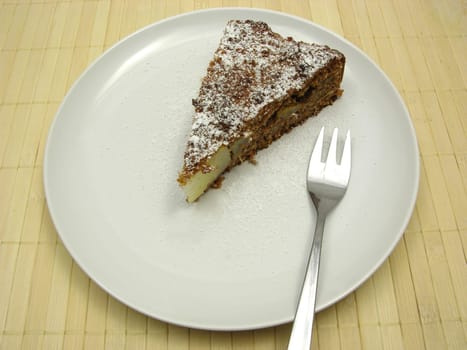 A piece of pear cake on a white plate dusted with powdered sugar