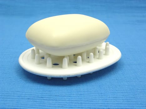 Beige soap on soap tray against light blue background