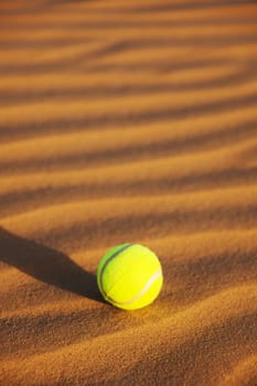 single yellow tennis ball in desert sand