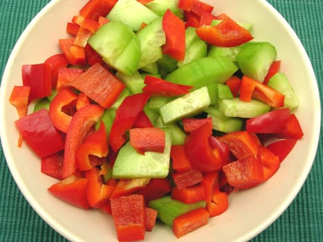 Cucumbers and pepper slices in a ceramic bowl against green background