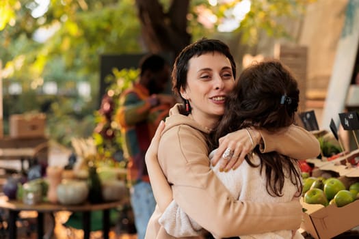 Friendly farm stand seller hugging happy loyal client before selling organic fruits and vegetables. Local grocery store owner greeting regular customer, being cheerful at food marketplace.