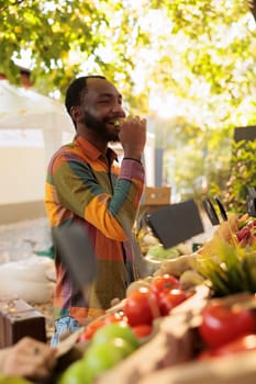 Smiling male person tasting apple before buying bio produce, shopping for natural organic products at farmers market. Young man customer enjoying food tasting fresh local produce.