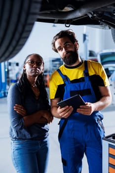 Proficient professional helping customer with car checkup in auto repair shop. Garage employee looking over automobile parts with woman, repairing her busted vehicle wheels during inspection