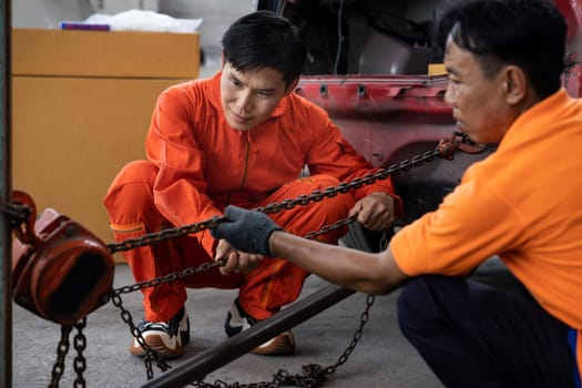 Mechanic testing strength and reliability of chain hoist for car towing in car workshop garage. Automotive service worker ensure through inspection of mechanical equipment. Oxus