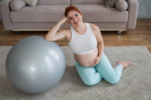 Pregnant woman resting after workout sitting on the floor near the fitness ball