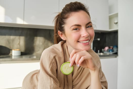 Food and lifestyle concept. Beautiful woman cooking in the kitchen, holding raw zucchini and smiling, preparing healthy vegetarian meal, making salad, looking happy.