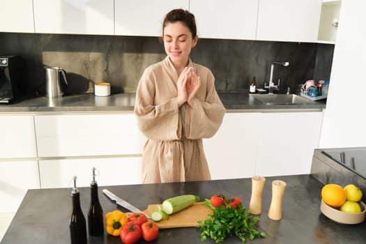 Portrait of woman in kitchen getting creative, thinking what to cook with vegetables, preparing healthy food, making dinner, looking at chopping board with zucchini and peppers.