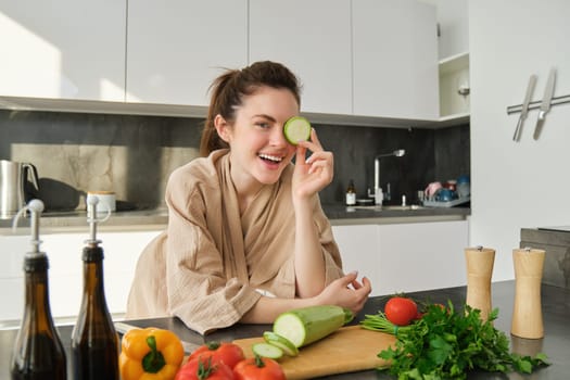 Portrait of brunette woman, wife cooking at home, making dinner, posing near chopping board in kitchen with vegetables, holding zucchini.