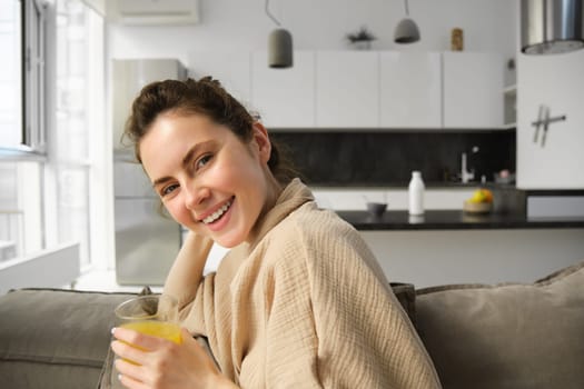 Women wellbeing and lifestyle. Beautiful young woman on sofa, drinking orange juice, relaxing at home on sofa, resting in the morning in living room.