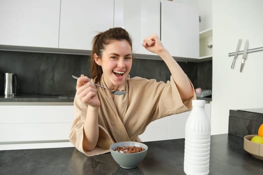 Portrait of happy, laughing young woman eating cereals with milk, triumphing, having breakfast and feeling excited, energetic morning concept.