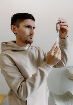 One young Caucasian handsome brunette man takes medicine from a bottle with a syringe to treat his cat, standing in the kitchen during the day, close-up side view.