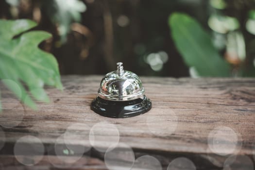 Hotel ring bell. Vintage bell to call staff outdoor in garden with green leaf, Closeup of silver service restaurant bell on wooden counter desk