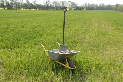 Wheelbarrow with gravel and spade on field