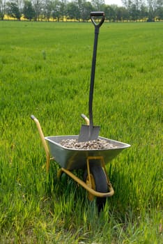 Wheelbarrow with gravel and spade on field