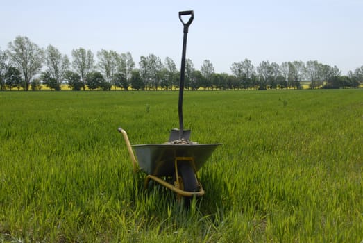 Wheelbarrow with gravel and spade on field