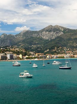 Sailing yachts and motorboats in the bay of Menton in front of the French mountain ranges