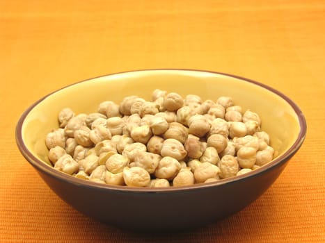 A ceramic bowl with chickpeas on an orange background
