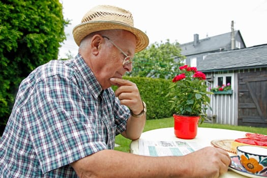 Senior sitting in garden and reading newspaper