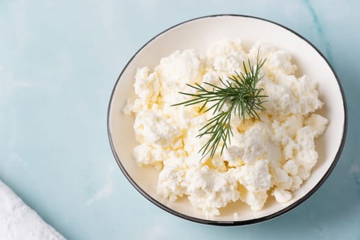 Fresh cottage cheese served in a bowl garnished with herbs on a clean kitchen surface.