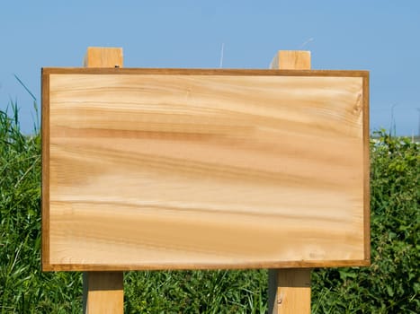Brown wooden blank sign infront of a green hedge and blue sky