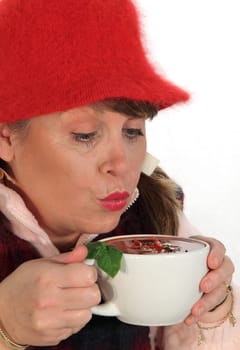 Middle aged woman cools her soup by blowing on it in cold weather.