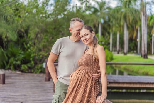 A happy, mature couple over 40, enjoying a leisurely walk in a park, their joy evident as they embrace the journey of pregnancy later in life.