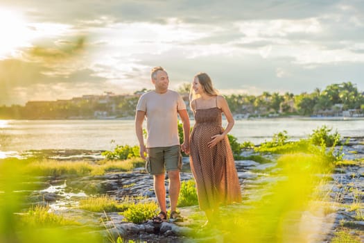 A happy, mature couple over 40, enjoying a leisurely walk on the waterfront On the Sunset, their joy evident as they embrace the journey of pregnancy later in life.