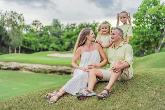 A happy family, two girls, dad, and a pregnant mom, enjoys quality time together on a lush green lawn, creating cherished memories of togetherness.