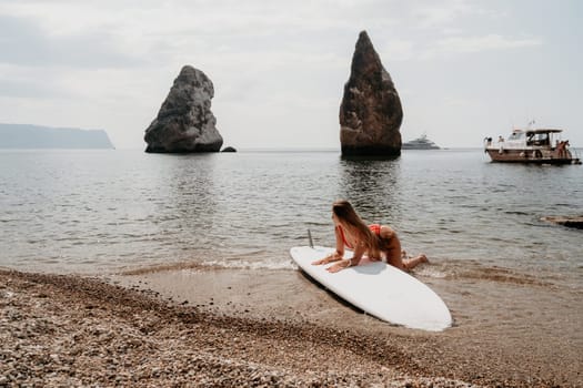 Close up shot of beautiful young caucasian woman with black hair and freckles looking at camera and smiling. Cute woman portrait in a pink bikini posing on a volcanic rock high above the sea