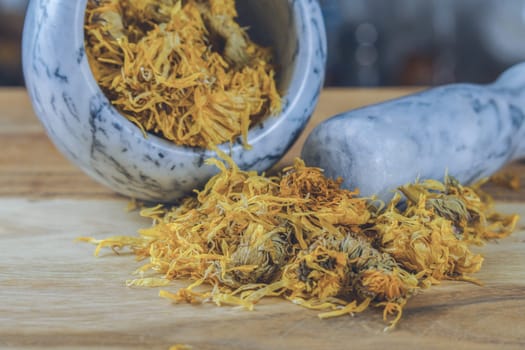 dried calendula flowers, Calendula officinalis, medicinal plant for therapeutic use, in a marble mortar on a wooden table and copy space