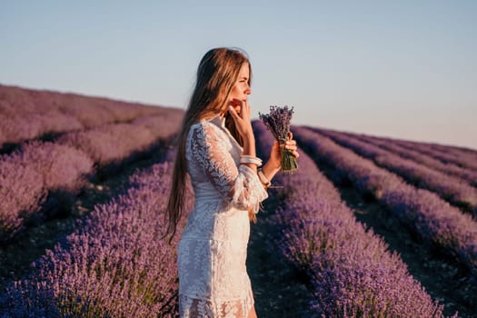 Close up portrait of young beautiful woman in a white dress and a hat is walking in the lavender field and smelling lavender bouquet.