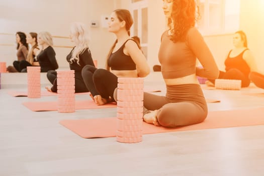 Group of young womans fitness instructor in Sportswear Leggings and Tops, stretching in the gym before pilates, on a yoga mat near the large window on a sunny day, female fitness yoga routine concept.