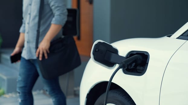 A man unplugs the electric vehicle's charger at his residence. Concept of the use of electric vehicles in a progressive lifestyle contributes to a clean and healthy environment.