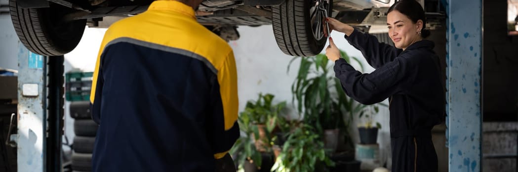 Vehicle mechanic conduct car inspection from beneath lifted vehicle. Automotive service technician in uniform carefully diagnosing and checking car's axles and undercarriage components. Panoram Oxus