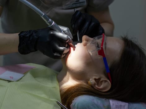 The process of removing braces. A beautiful woman in protective glasses in a dental chair during the procedure of removing braces from teeth. Dentist and assistant working.