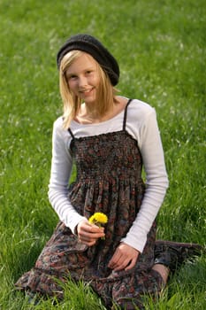 a young,blond and laughing girl sits in the grass with a flower