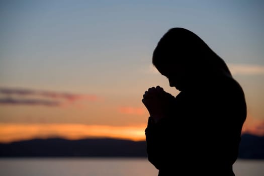 A teenage girl prays at sunset