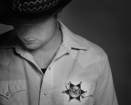 Cowboy looking down under hat with Sheriff's badge on shirt