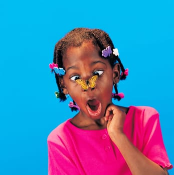 African little girl with butterfly barrettes and a butterfly on her nose looking surprised
