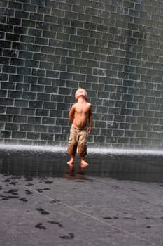 A boy standing beside a wall fountain, Chicago, Illinois, USA