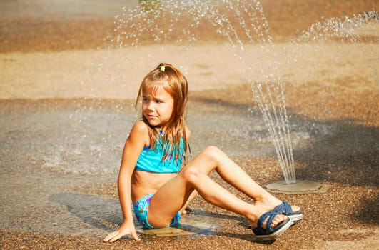 Child sits beside sprinkler