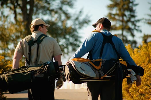 Two men carry golf bags