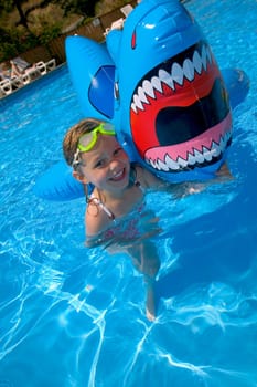 Girl playing in swimming pool with inflatable shark