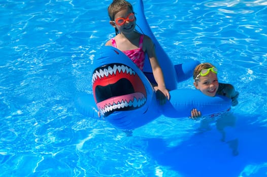 Girls playing in swimming pool with inflatable shark