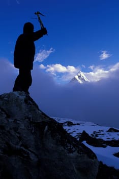 Mountaineer on peak with mountain peak rising out of clouds in background
