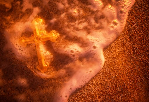 Cross being washed over by wave on sandy beach