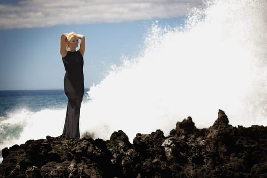 Woman in evening dress standing on the rocks as the surf breaks
