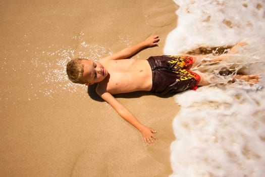 Boy lying on beach in water