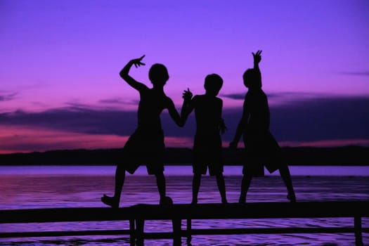 Three silhouettes of boys on a dock against a sunset