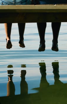 Two people dangling their feet off a dock
